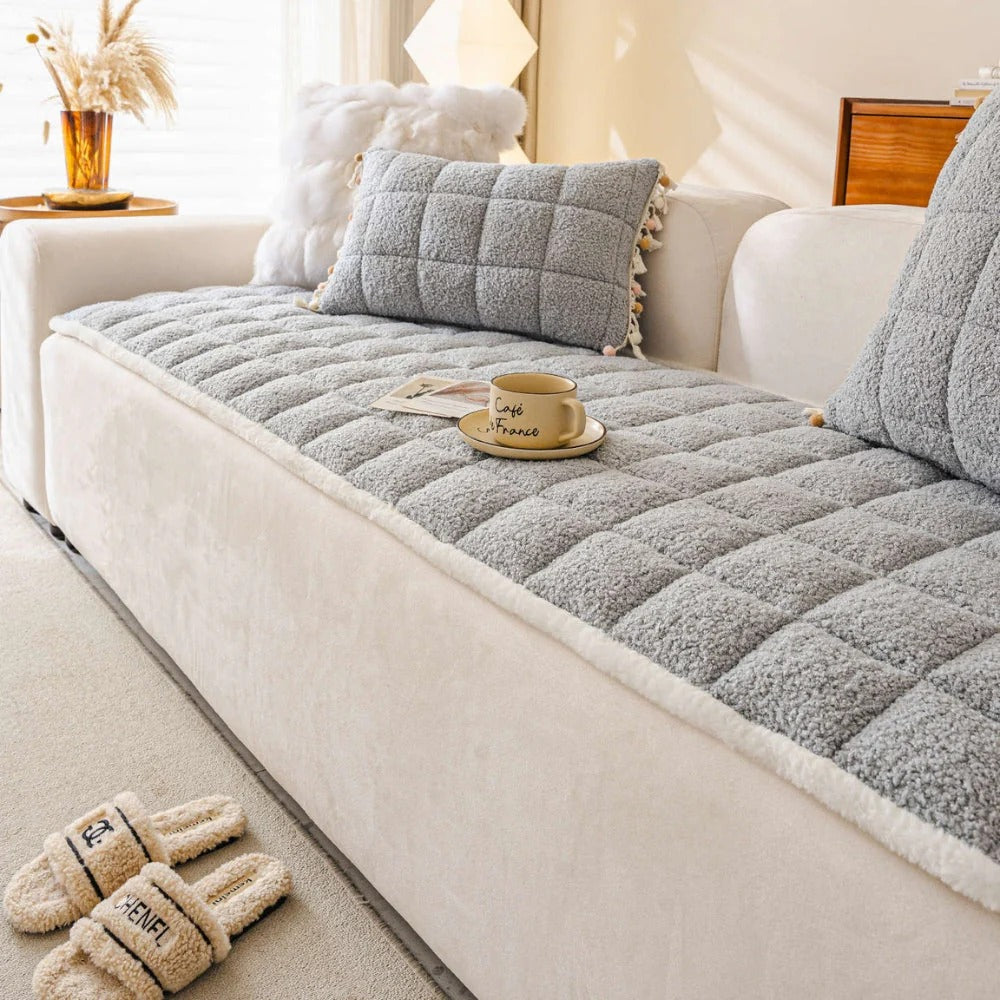 Gray quilted sofa cover on a white sofa with a cup and saucer, slippers, and decorative pillows in a cozy living room.