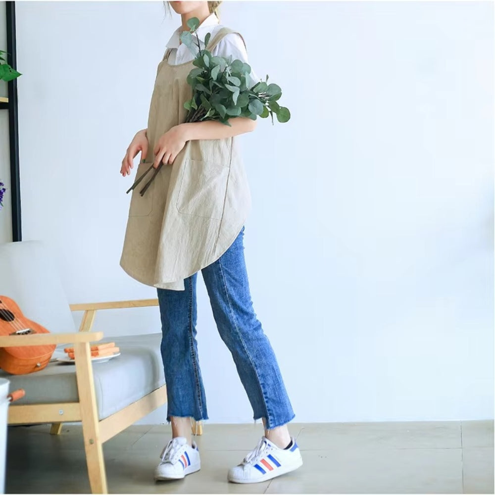 Person wearing a beige apron holding greenery indoors with a guitar and chair in the background.