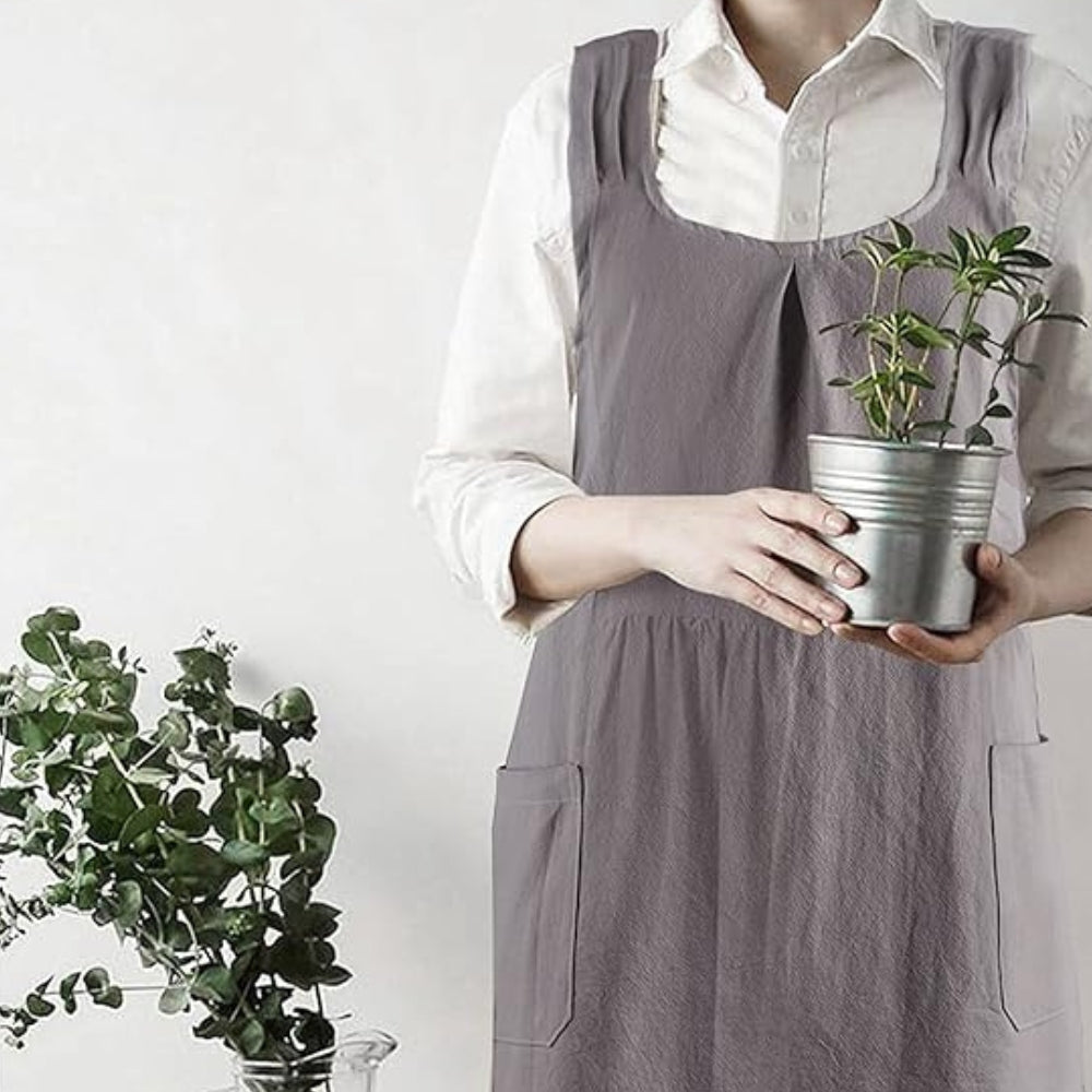 Person wearing a gray apron holding a potted plant against a white background