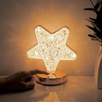 Star-shaped lamp with a hand touching it on a reflective surface.