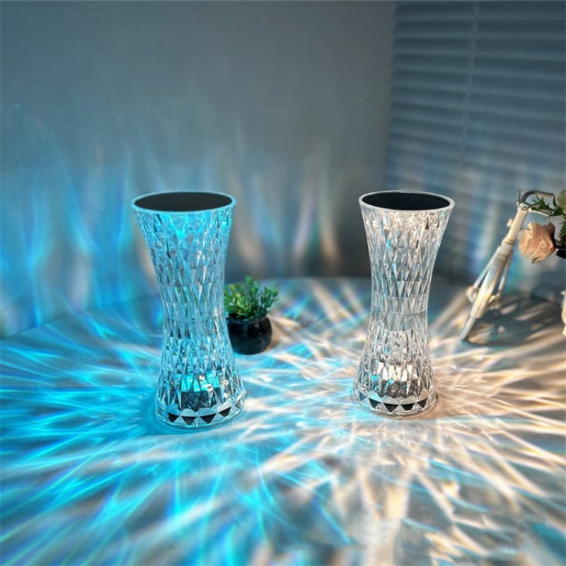 Two illuminated glass vases on a reflective surface with a blurred background