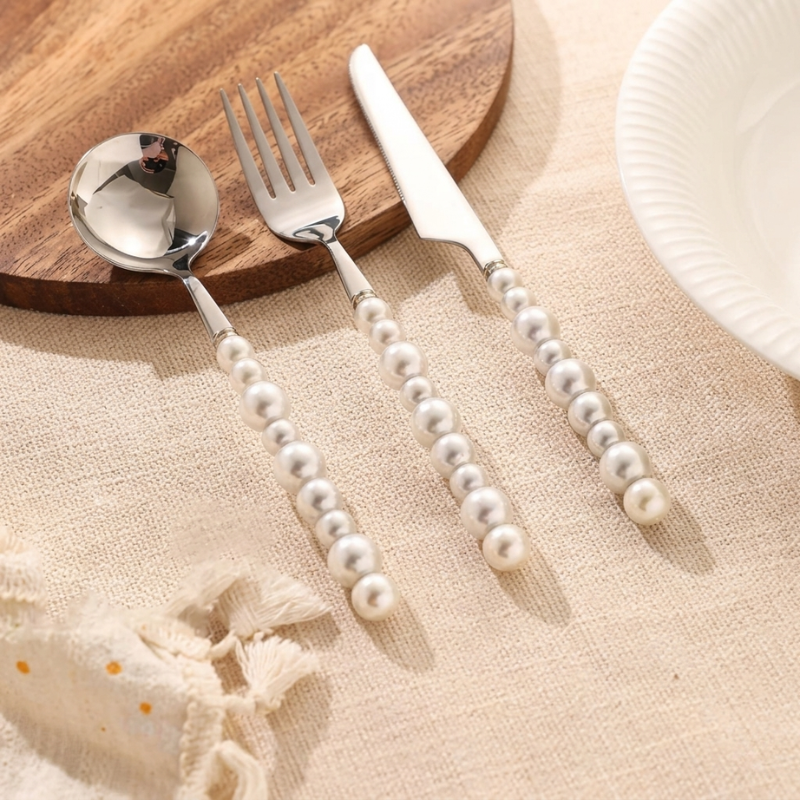 Silver cutlery set with pearl handles on a wooden board and beige surface.