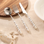 Silver cutlery set with pearl handles on a wooden board and beige surface.