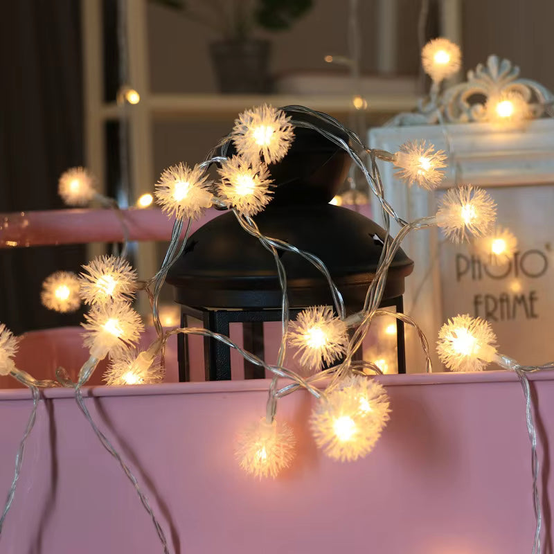 Decorative string lights with flower-shaped bulbs on a pink surface.