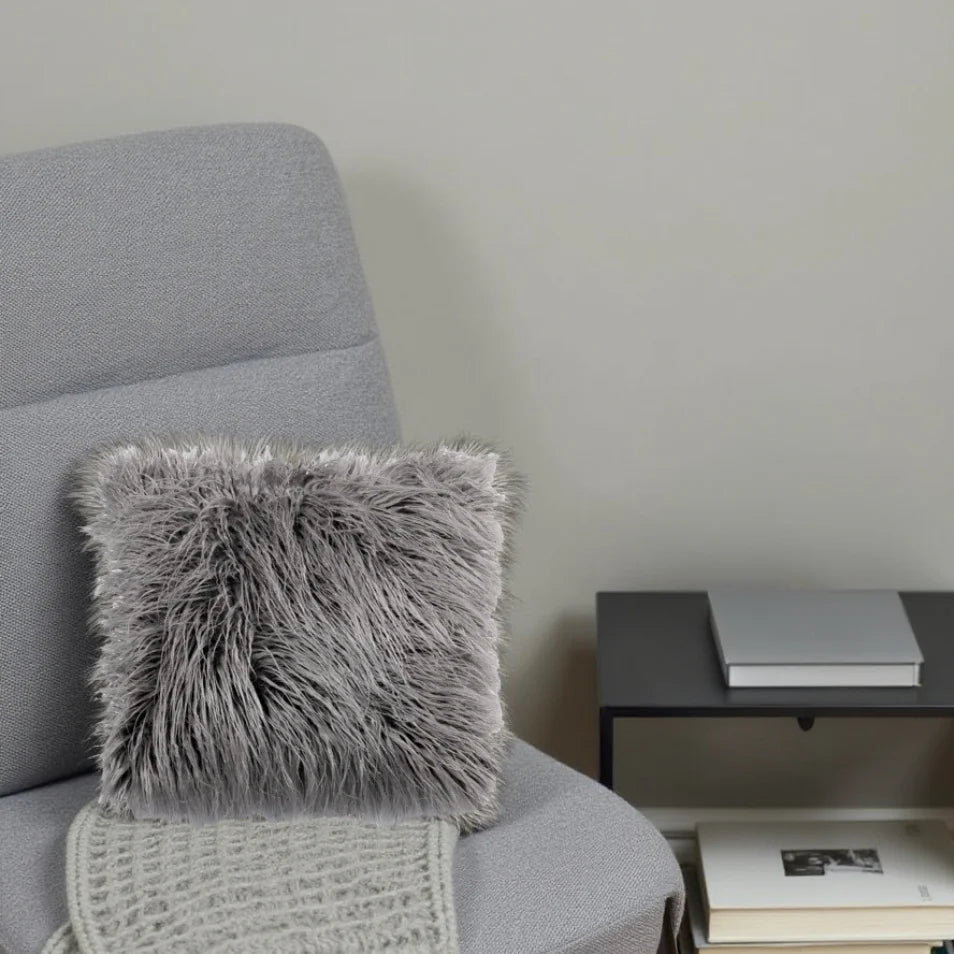Gray armchair with a fluffy gray pillow and a side table with books against a plain wall.