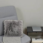 Gray armchair with a fluffy gray pillow and a side table with books against a plain wall.