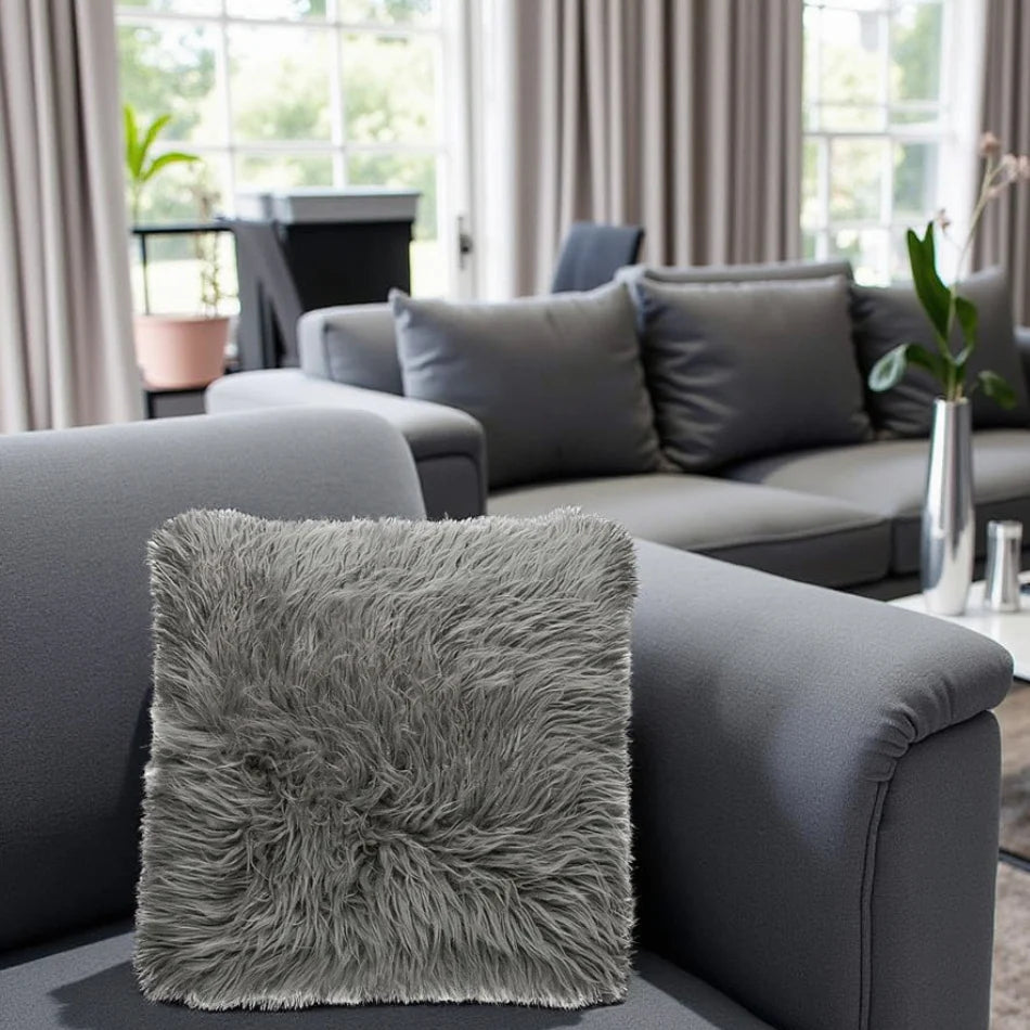 Gray fluffy pillow on a gray sofa in a living room with curtains and plants.