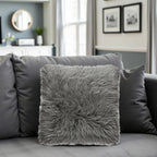 Gray fluffy pillow on a gray sofa in a living room setting.