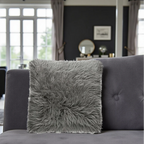 Gray fluffy pillow on a gray sofa in a living room setting.