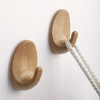 Two wooden wall hooks on a white background with a white rope hanging from one of them.