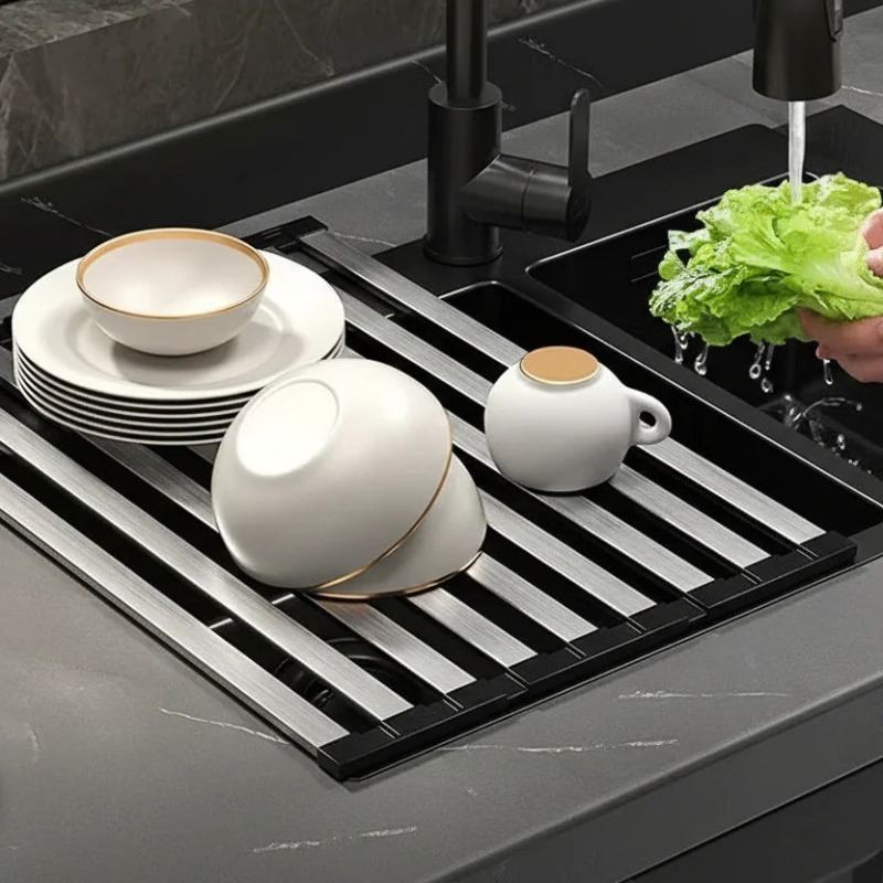 Kitchen sink with a drying rack holding dishes and a person washing vegetables.