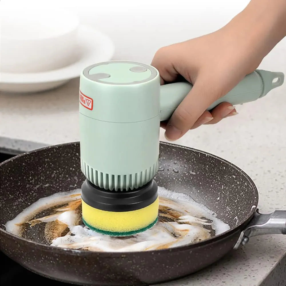 Hand using a green electric scrubber to clean a frying pan on a kitchen counter.