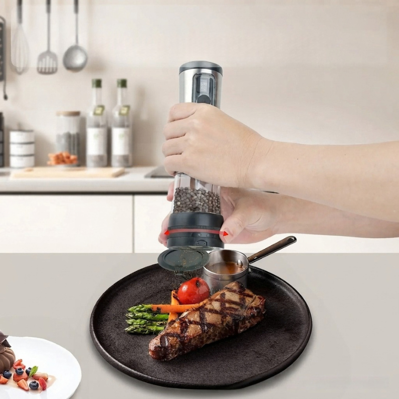A hand holding a manual electric pepper mill grinder over a plated steak in a kitchen setting.