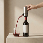 Hand using a wine aerator to pour red wine into a glass on a neutral background