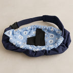 A padded waist bag or fanny pack in navy blue fabric with a light blue patterned inner lining featuring white nautical motifs. The bag has a black plastic buckle and a black fabric loop on the front, photographed on a neutral beige background.
