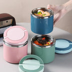 Three colorful stainless steel food containers with lids on a light surface.
