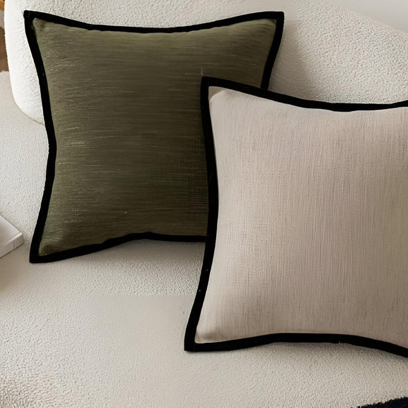 Two decorative pillows with black trim on a light-colored sofa.