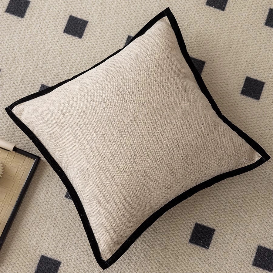 Beige pillow with black trim on a patterned rug