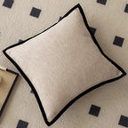 Beige pillow with black trim on a patterned rug