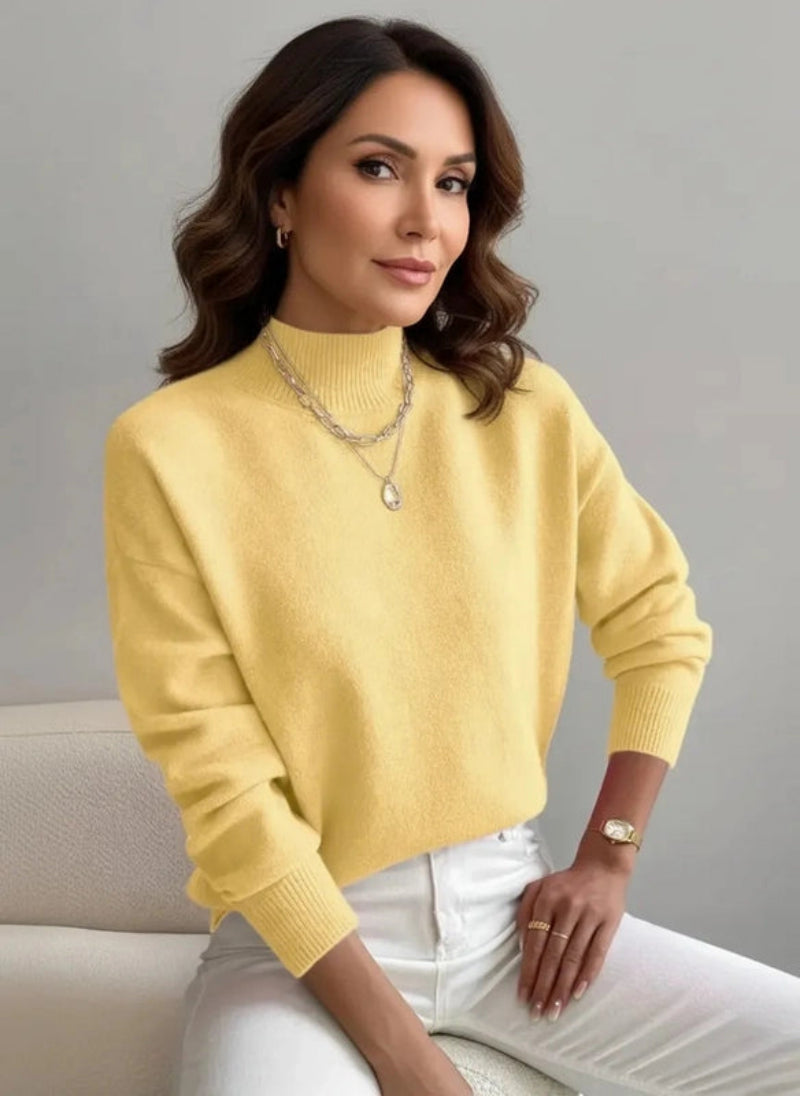 Woman wearing a yellow sweater and white pants sitting on a gray background