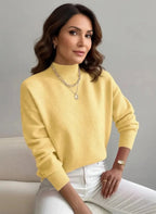 Woman wearing a yellow sweater and white pants sitting on a gray background