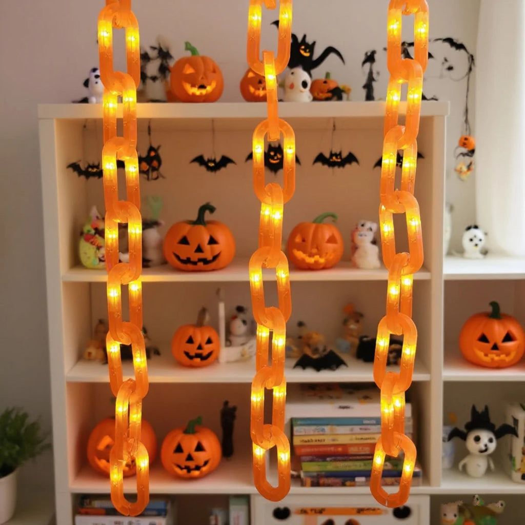 Orange hanging chain lights with warm white LED bulbs, shown hanging in front of a white shelving unit filled with Halloween decorations and jack-o'-lanterns.