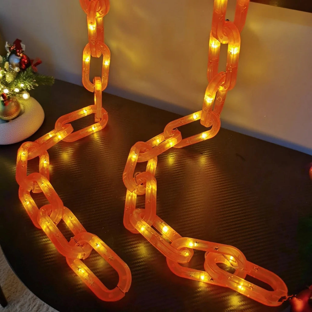 Orange translucent chain holiday lights with warm white LED bulbs, draped across a dark table with a softly lit indoor background.
