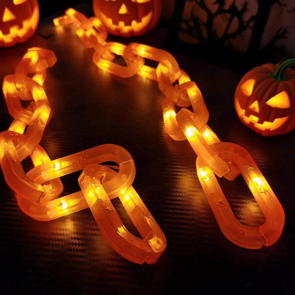 A glowing orange LED chain link Halloween decoration displayed on a dark surface, with carved jack-o'-lanterns in the background.