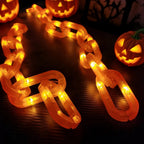 A glowing orange LED chain link Halloween decoration displayed on a dark surface, with carved jack-o'-lanterns in the background.