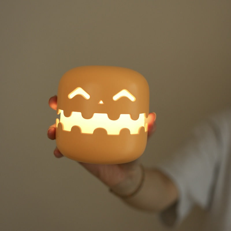 Hand holding a small glowing jack-o'-lantern-like lantern with a neutral background