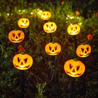 A set of glowing jack-o'-lantern pumpkin garden lights with carved faces, mounted on black stakes and arranged in a dark garden at night.