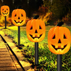 Four glowing jack-o'-lantern Halloween yard lights on black stake posts, arranged along a grassy lawn next to a paved walkway at night.