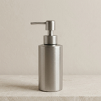 Metallic soap dispenser on a beige surface with a neutral background