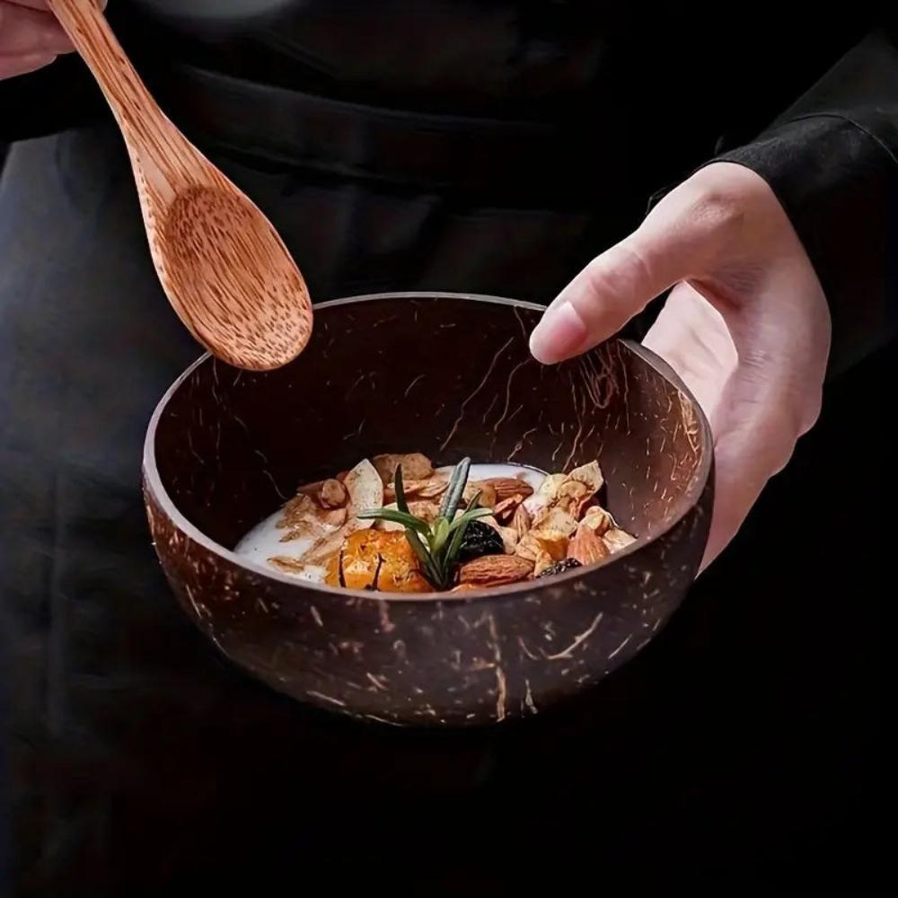 Coconut bowl with a cereal-like dish, wooden spoon, and hand holding the bowl against a dark background