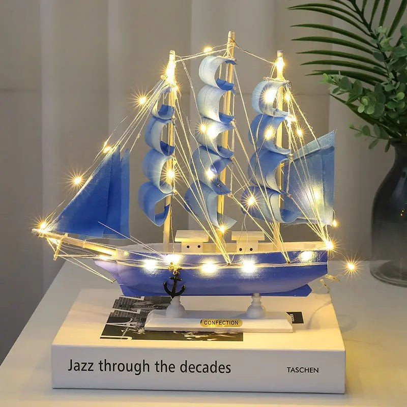 Decorative ship model with lights on a book, placed on a surface with a plant in the background.