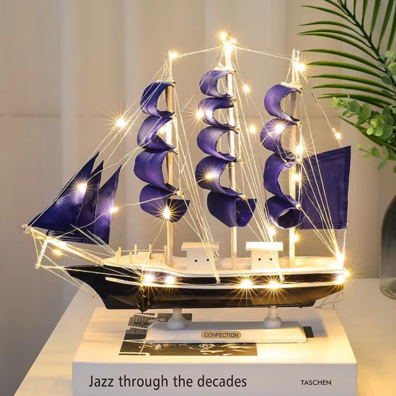 Decorative model ship with purple sails and string lights on a white surface.