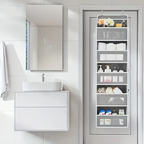 A white hanging door organizer shelf mounted on a bathroom door, shown with folded towels, toiletries, and small decor items. The bathroom features a white vanity, sink, mirror, and tiled wall.
