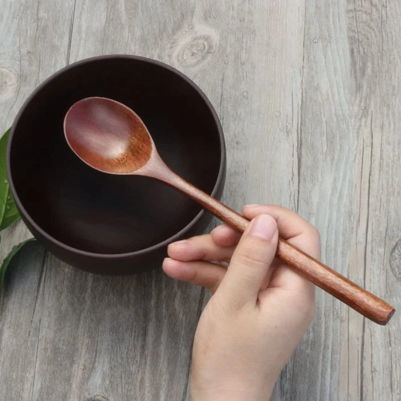 Hand holding a wooden spoon over a dark bowl on a wooden surface