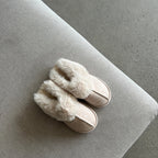 Pair of white slippers with fluffy fur trim on a gray surface