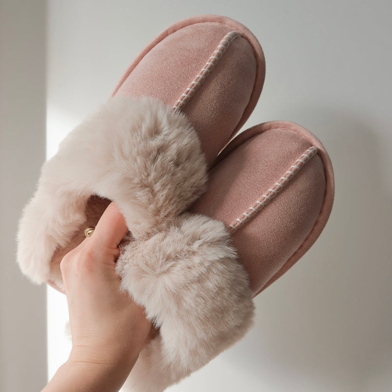Pink slippers with fluffy fur trim held by a hand against a neutral background