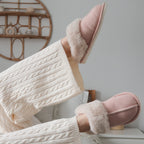 Person wearing pink slippers with fluffy interior and white cable-knit pants in a cozy setting.