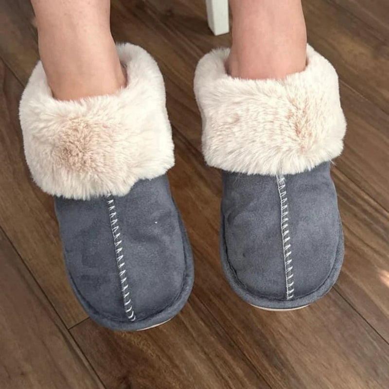Gray slippers with white fur trim worn indoors on a wooden floor.