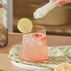 Pink cocktail with lime garnish on a green patterned coaster, with a blurred background.