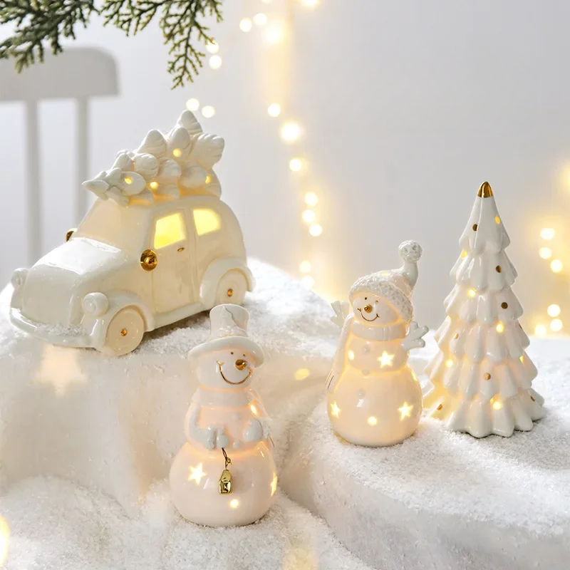 Decorative Christmas scene with a car, snowman, and tree on a snowy surface with lights in the background.