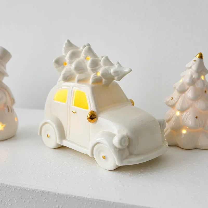 White ceramic car with a Christmas tree on top, surrounded by other decorative items on a light gray background.