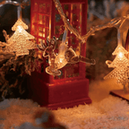 Warm white Christmas string lights featuring a red telephone booth, a reindeer, and gold glittery tree ornaments, shown in a cozy holiday setting with snow-like white faux snow.