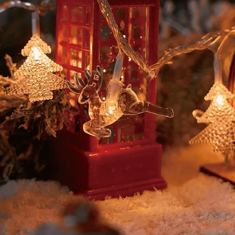 Warm white Christmas string lights featuring a red telephone booth, a reindeer, and gold glittery tree ornaments, shown in a cozy holiday setting with snow-like white faux snow.