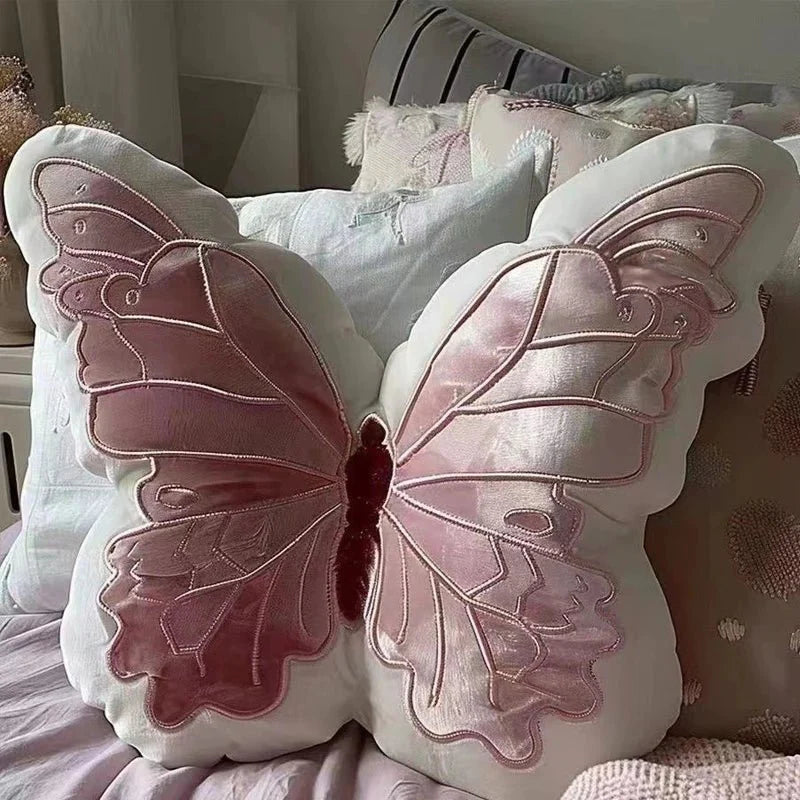 Butterfly-shaped pillow with pink wings on a bed
