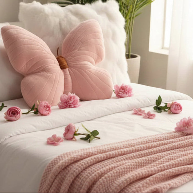 Pink butterfly-shaped pillow on a bed with pink flowers and a pink blanket.