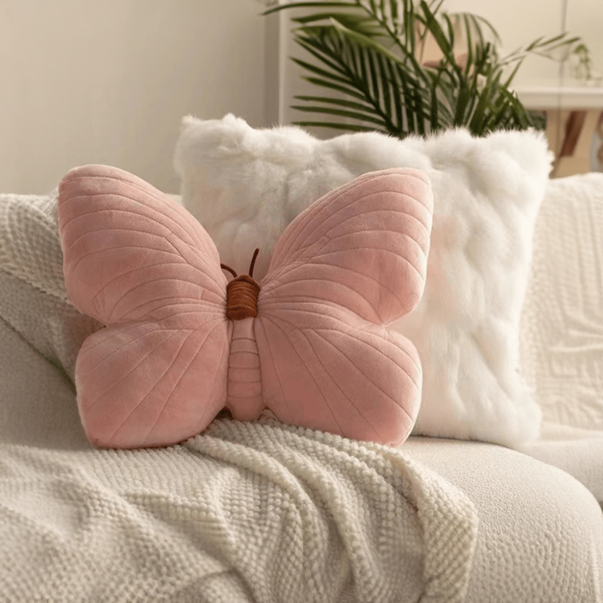 Pink butterfly-shaped pillow on a couch with a neutral background